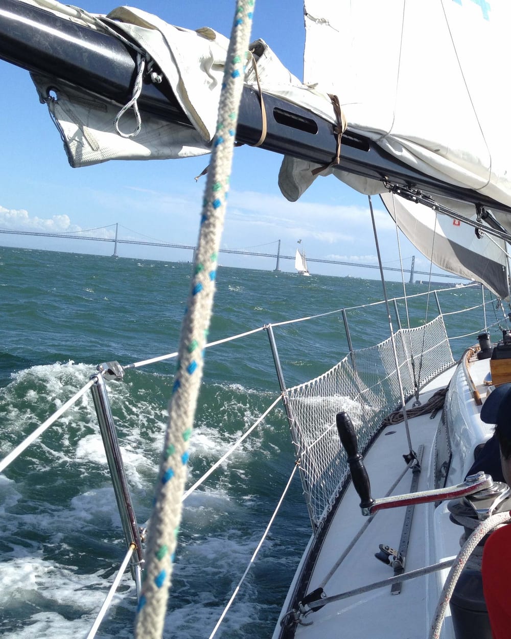 Looking forward along the deck of Yukon Jack as she heels in a stiff breeze, white water rushing past the bow and the Bay Bridge in the distance