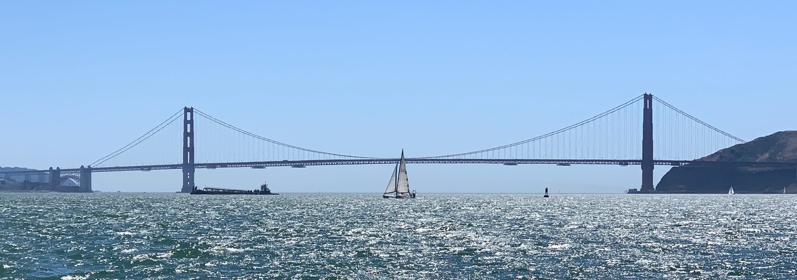 The Golden Gate Bridge seen across the water, with a single sailboat passing under the middle of the span