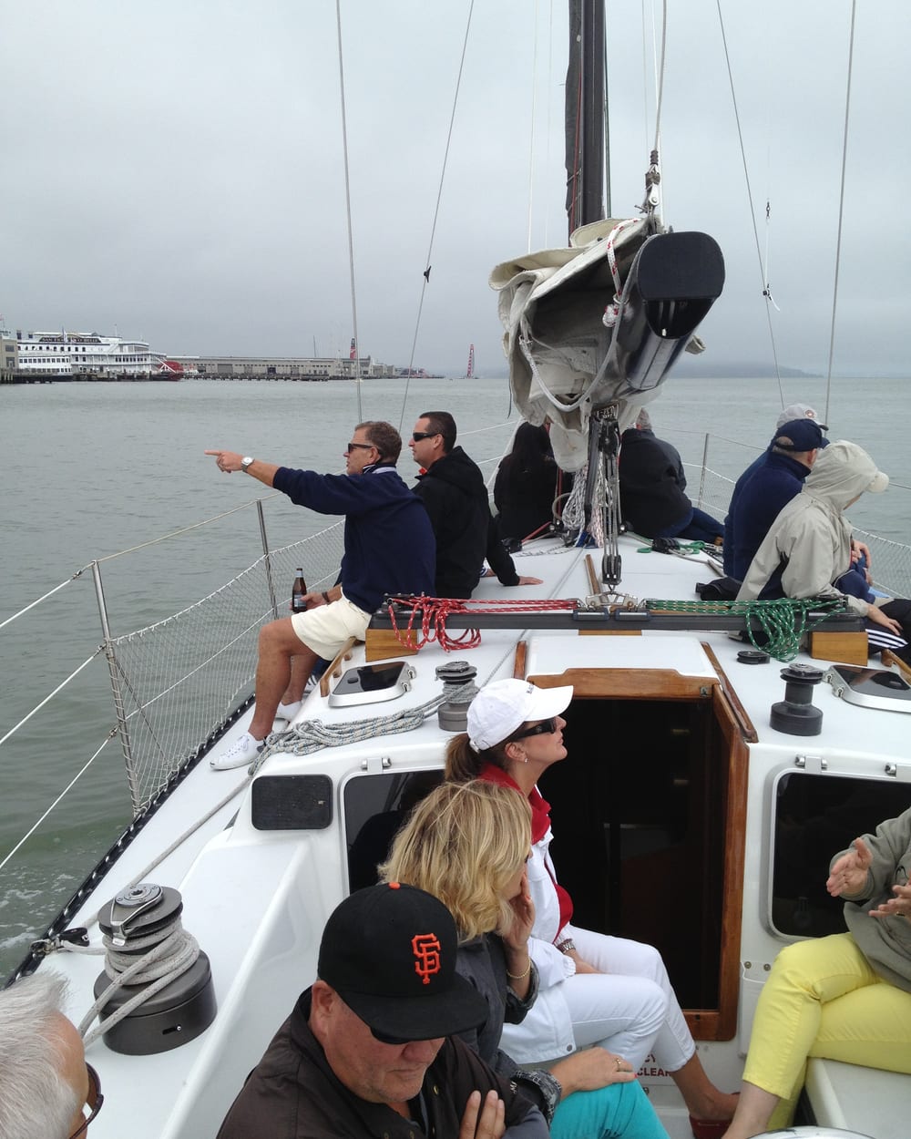 Guests in jackets and hoods sitting on the foredeck of Yukon Jack under a flat grey sky, one pointing toward the city waterfront
