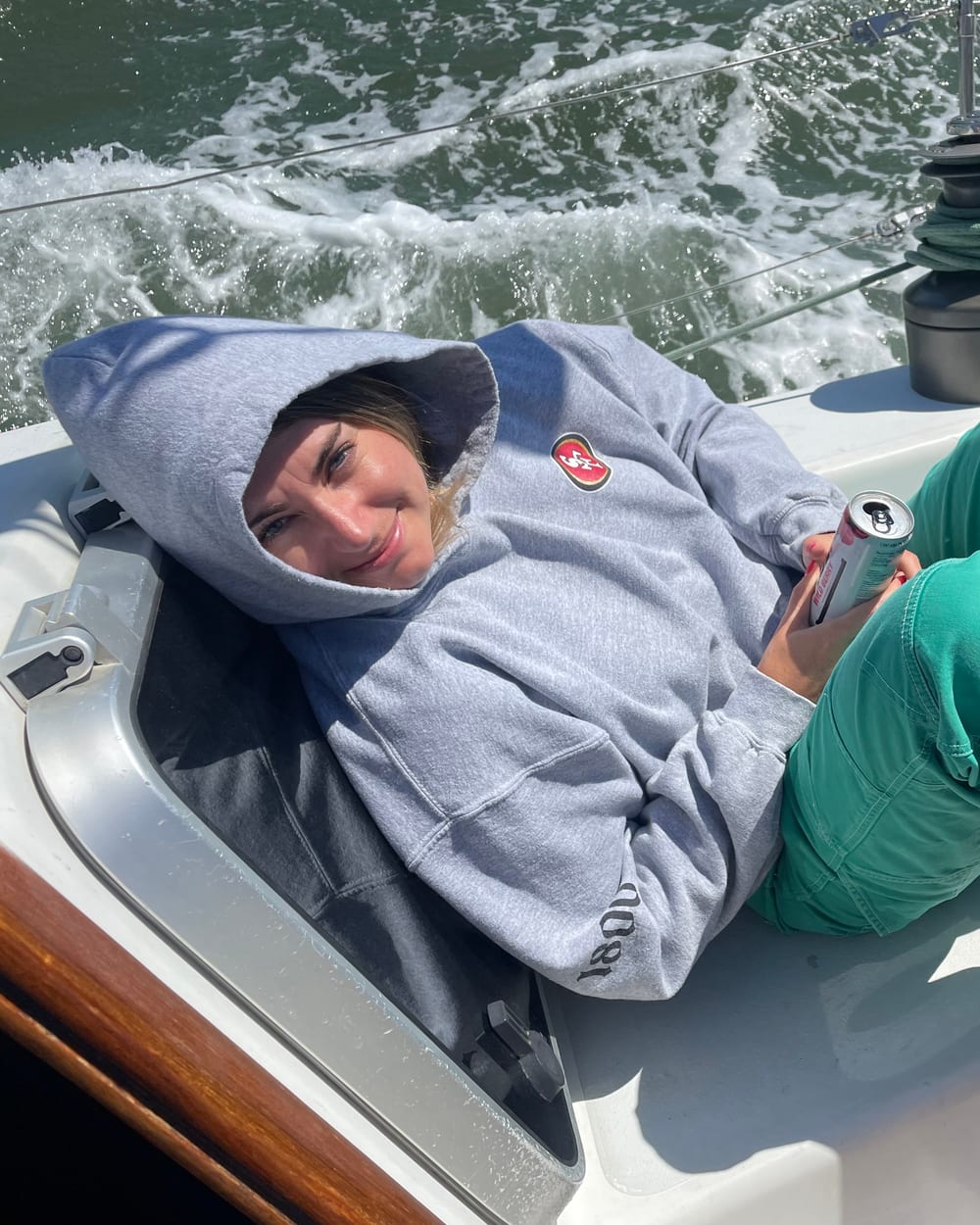 A guest with a grey hoodie pulled up over her head, smiling as she leans back in the cockpit of Yukon Jack, with white water rushing past